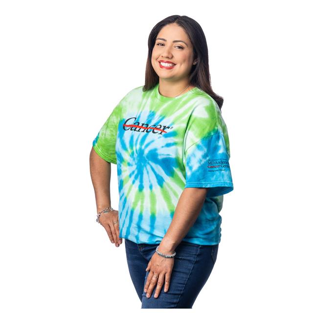 MD Anderson employee wearing a green and Blue Tie-Dye shirt featuring the black cancer strikethrough logo on the chest and the black MD Anderson logo on the sleeve.