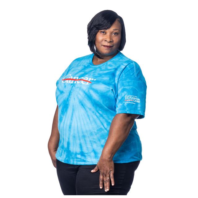 MD Anderson employee wearing a turquoise Tie-Dye shirt featuring the white cancer strikethrough logo on the chest and the full white MD Anderson logo on the sleeve.
