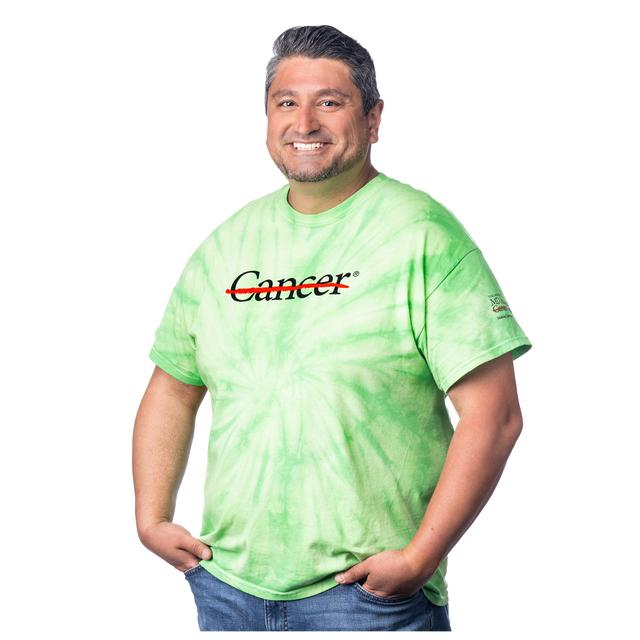 MD Anderson employee wearing a lime Tie-Dye shirt featuring the black cancer strikethrough logo on the chest and the full black MD Anderson logo on the sleeve.