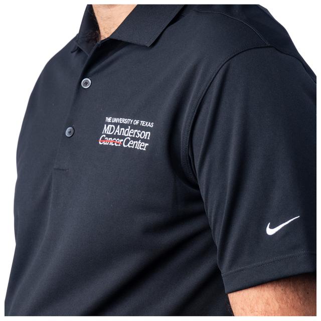 Closeup of MD Anderson employee wearing a black Nike Dri-Fit polo featuring the white MD Anderson logo on the chest area and the Nike logo on the sleeve.