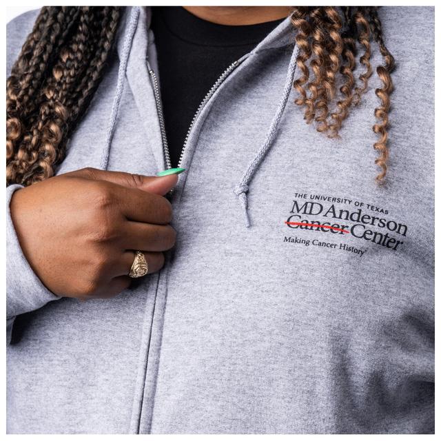 Closeup of MD Anderson employee wearing the grey zippered hoodie with pockets, featuring the black MD Anderson logo on the chest area.