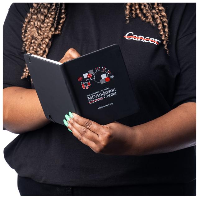 MD Anderson employee holding a black notebook featuring the research logo with the white MD Anderson logo displayed at the bottom.